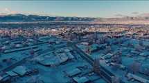 Aerial View Flying Over Snow-Covered Town With Mountains In Distance