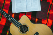 guitar, Bible, and journal on a plaid blanket 