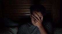 a stressed man looking at a computer screen and covering his face with his hands 