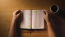 An overhead shot of a man flipping through his bible at a table with coffee