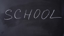 Bold white chalk letters spell School. Inscription SCHOOL. Chalk writing on blackboard. Concept of beginning of school year.	