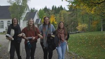 Group of young women walking towards camera, arms linked and smiling 