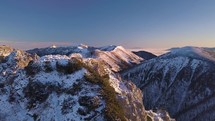 Fly above alps mountains summit with man stands on the top of rocky mountain peak in cold sunny winter day