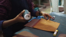 Woman putting glue on a leather wallet in a leather goods workshop