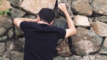 man pounding his fist against a stone wall 