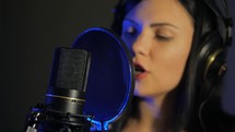 young woman sings a song near a microphone in a recording studio under natural light. Close-up face. 4k