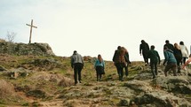 a group of people walking up a mountainside towards a cross 