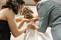 Two women help a bride button her wedding dress.