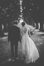 A bride and groom walking hand-in-hand down a country lane.