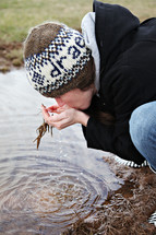 A woman scoops water and drinks from a stream.