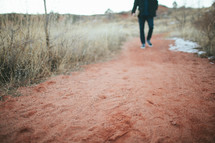 man walking down a red dirt road 
