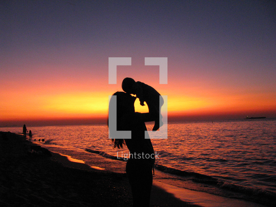 silhouette of a mother holding her toddler on a beach at sunset 