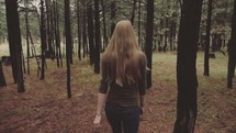 Back of a woman walking through the trees in the woods.