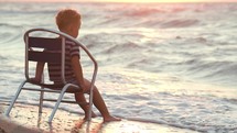 Boy sitting alone on the chair by sea