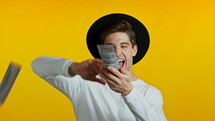 Man in white with surprised happy face scatters, waste money. Person overspend US currency. Guy is flush with dollars on yellow studio background . High quality 4k footage