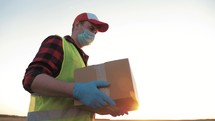 Delivery concept. Courier with parcel. Delivery man holding package in his hands while wearing face mask for coronavirus. Delivery man holding cardboard boxes in medical rubber gloves.