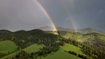 Aerial view of beautiful double rainbow over green forest country