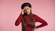 Young woman having headache, studio portrait. Girl putting hand on head, displeased rolling eyes. isolated on pink background. Concept of problems, depression