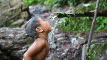 Boy washing and drinking from water running from a tree.