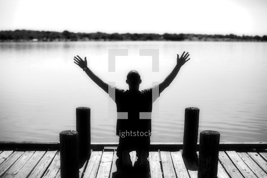 Man kneeling with raised hands on river dock