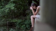 Praying woman sitting on a ledge by a pond.