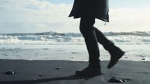 a man in a coat and boots walking on a beach in winter 