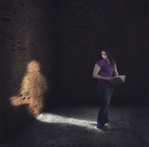 Woman standing in the light of her own shadow holding a Bible.