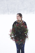 a woman standing outdoors in the snow holding a Christmas wreath 