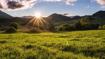 Sunset time lapse in green countryside nature with grass meadow in foreground in sunny summer evening landscape
