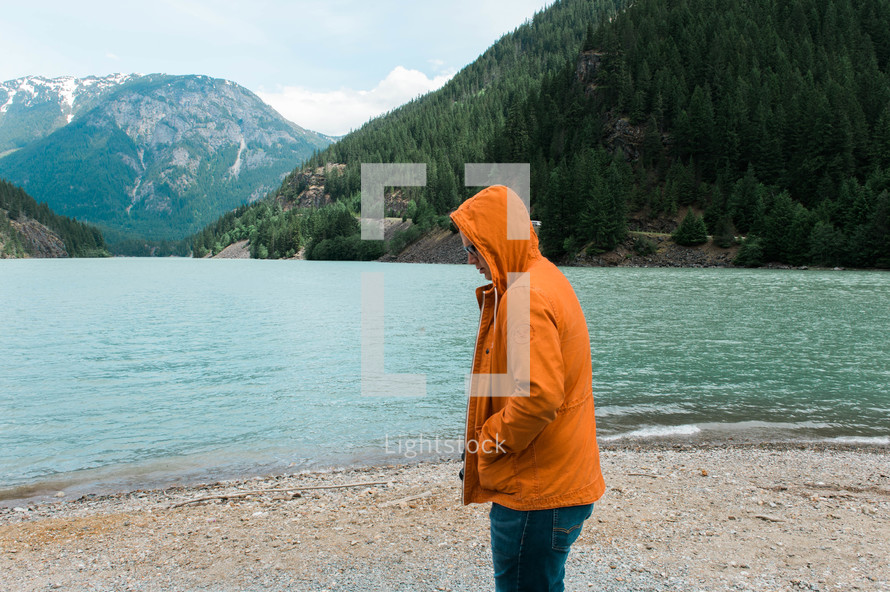 a man in an orange jacket standing on a lake shore 