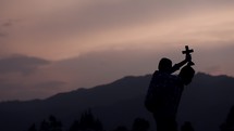 father and son holding a cross on a mountaintop at sunrise 