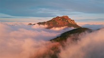Misty mountain hidden in foggy clouds, sunrise golden colors, Aerial view fly back peaceful alpine nature
