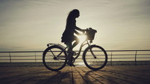Silhouette of woman riding bike near the sea