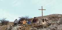 group of people walking up the side of a mountain towards a cross 