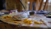Wooden art palette with oil paints. Mixing colors together. Artistic instrument with many colors. Working tool with squeezed out tubes of paint.