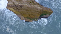 Top aerial drone view of waves crashing on rocky coastline