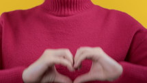 Unrecognizable woman showing sign of shape heart. Yellow background. Women health, volunteering, charity donation, help and trust relationships concept. High quality 4k footage