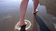 Legs of woman walking barefoot on wet black volcanic sandy island beach. Beautiful feet of young girl near sea on sunset or sunrise. Slow motion. High quality 4k footage