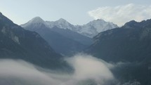 Aerial drone flying through the misty mountains with small chalet and homes below