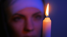 Woman nun praying at night. burning candles. Woman in clothes nuns. Blurry face, focus on fire of candle.