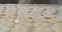 Baker sprinkling powdered sugar onto a sheet of cookies.