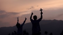 father and son holding a cross on a mountaintop at sunrise 