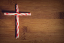 A cross made from peppermint sticks on a wooden table.