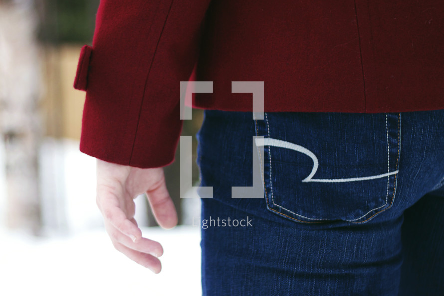 A woman in blue jeans and a red coat.