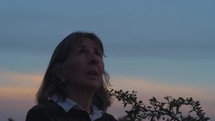 A woman praying earnestly outdoors at dusk