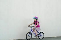 A young girl in a helmet rides a purple bicycle.