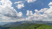 White clouds towering over blue sky and green forest landscape time lapse
