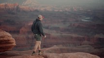 Male hiker walks to the edge of a cliff and admires stunning canyon views during sunset