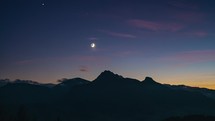 Blue night sky with moon and stars above alpine mountains nature in summer evening landscape Time lapse
