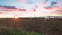 High speed white and red train passing against a beautiful sunset sky in the countryside.